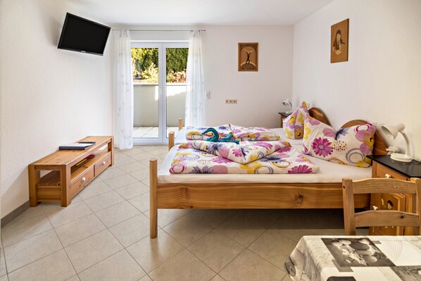 A bedroom with a bed, a wooden nightstand, a TV mounted on the wall, and a sliding glass door leading to an outdoor area.