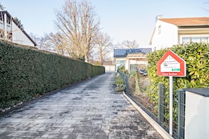 A paved pathway leading to a gated residential area with a solar panel-equipped building in the background.