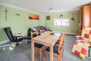 A room with a dining table, chairs, a sofa, a massage chair, and a window with a view.