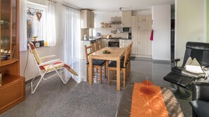 Une cuisine moderne avec des meubles en bois, un coin repas avec une table et des chaises, un canapé en cuir noir et un meuble vitrine en verre.