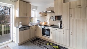Une cuisine moderne avec des meubles en bois clair, des appareils en acier inoxydable et une grande fenêtre.