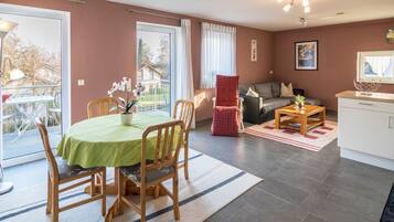 Ein Wohnzimmer mit Esstisch, Stühlen, einer Couch, einem Couchtisch und einem kleinen Schrank.