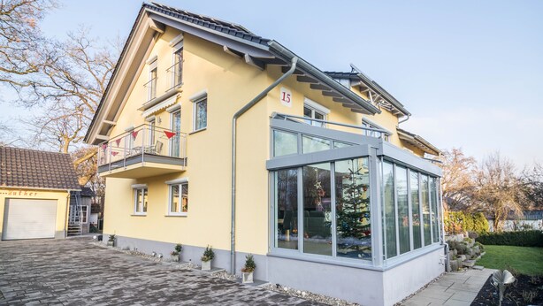 Ein zweistöckiges Haus mit Balkon, Garage und Wintergarten.