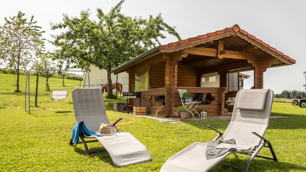 A wooden cabin with two lounge chairs, a table, and a covered porch. - Holiday Apartment 1 on “Wagenberg” Farm with Mountain View, Wi-Fi & Garden (Deggenhausertal)