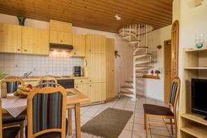 A kitchen with wooden cabinets, a dining table with chairs, a spiral staircase, and a television on a wooden stand.