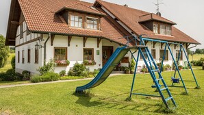 A house with a steeply pitched roof, a front porch, and a swing set. - Holiday Apartment 1 on “Wagenberg” Farm with Mountain View, Wi-Fi & Garden (Deggenhausertal)