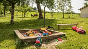 A sandbox with toy vehicles and a picnic table in a grassy area with trees and a barn in the background. - Holiday Apartment 1 on “Wagenberg” Farm with Mountain View, Wi-Fi & Garden (Deggenhausertal)