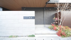 A modern hotel entrance with a wooden canopy, a stone wall, and a signboard. - Hotel Rokune (Nara)