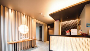 A reception area with a wooden reception desk, a round mirror, and a patterned partition. - Hotel Rokune (Nara)