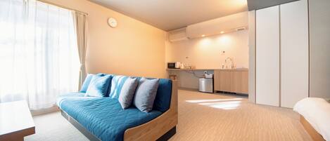 A modern hotel room with a large bed, a desk, a kitchenette, and a wardrobe.