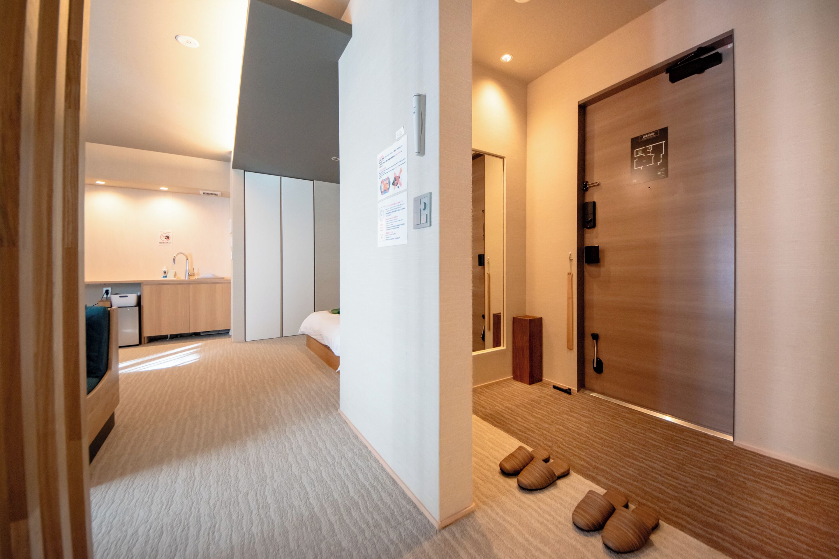 Une chambre d’hôtel comprenant un lit, un petit bureau, une chaise, une armoire et une salle de bain avec un lavabo et un miroir.