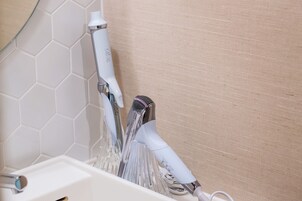 Un baño con un lavamanos blanco, un espejo y una ducha con manguera blanca.