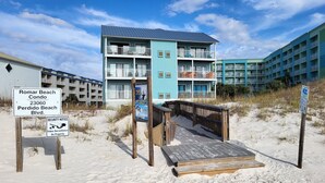 A multi-story building with balconies, a beach boardwalk, and signs indicating a security notice and surveillance.