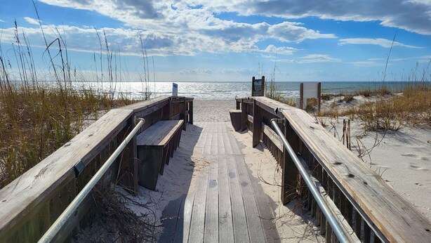 A wooden boardwalk leading to a beach with a clear view of the ocean.