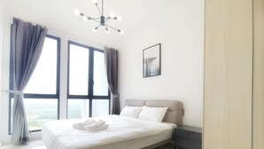 A modern bedroom with a large bed, a nightstand, a bedside table, and a view of the city through large windows. - The Elysia Park Residence (Iskandar Puteri)