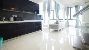 A modern kitchen with black cabinets, a white countertop, and a built-in microwave. There is a white sofa and a staircase in the living area. - The Elysia Park Residence (Iskandar Puteri)
