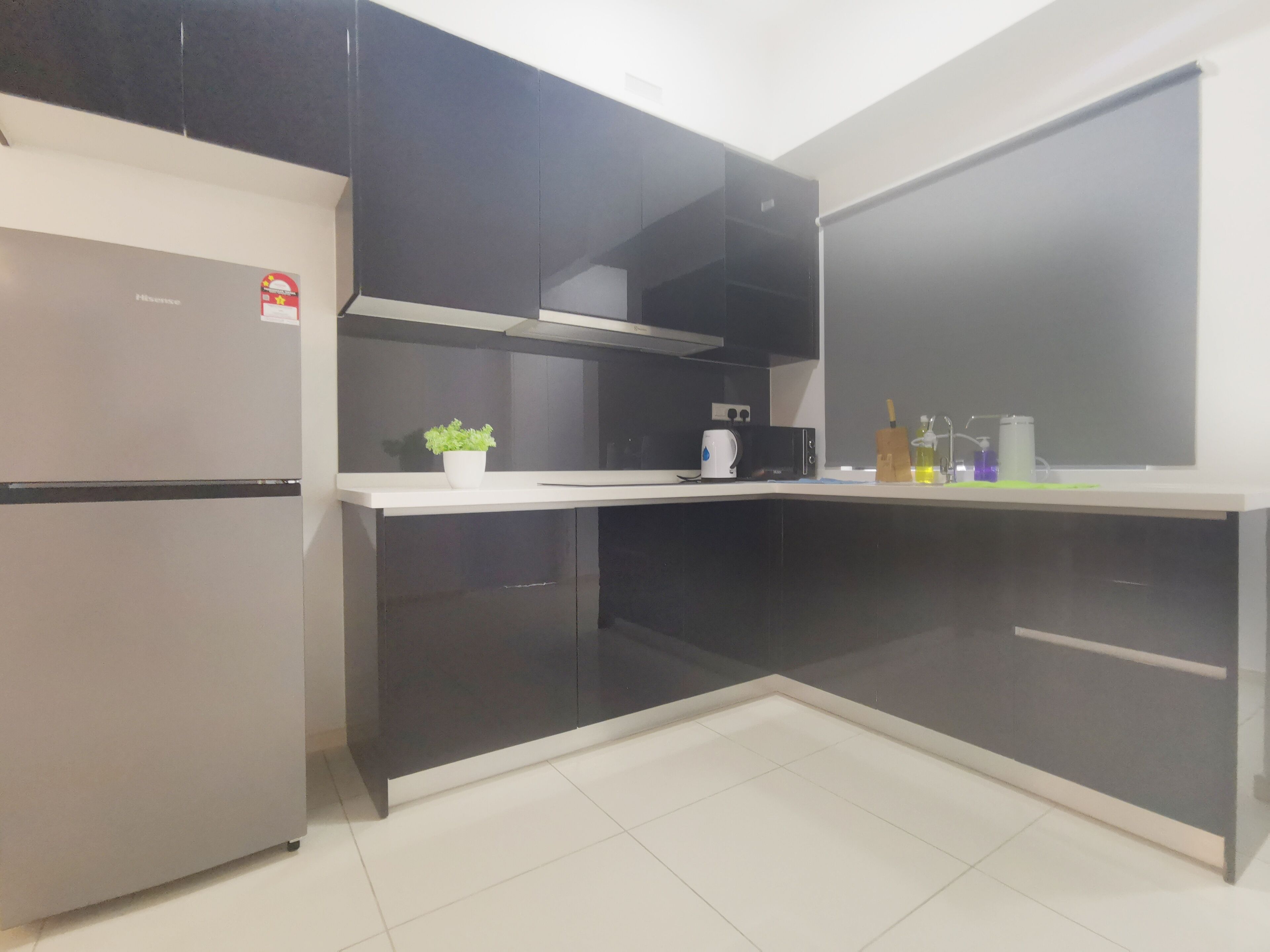 A modern kitchen with black cabinets, a stainless steel refrigerator, and a white countertop.