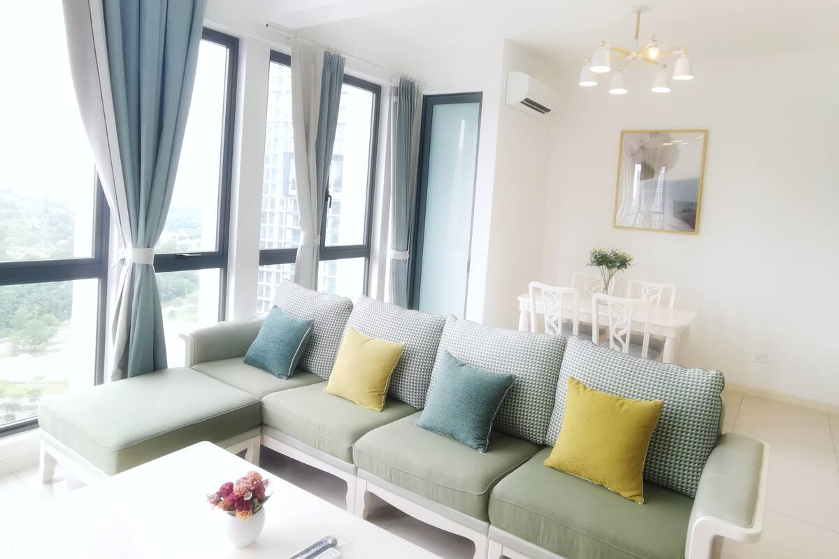 Un salon moderne avec un canapé d’angle, une table basse blanche et un coin repas avec des chaises blanches.