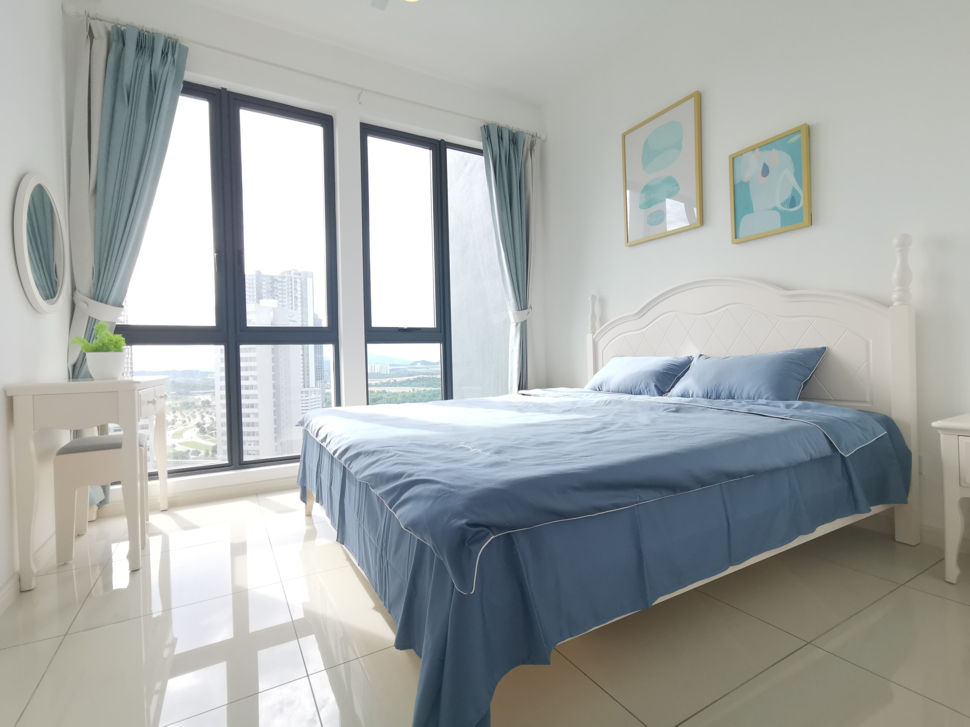 Un dormitorio con una cama grande, un escritorio y vistas a la ciudad a través de amplios ventanales.