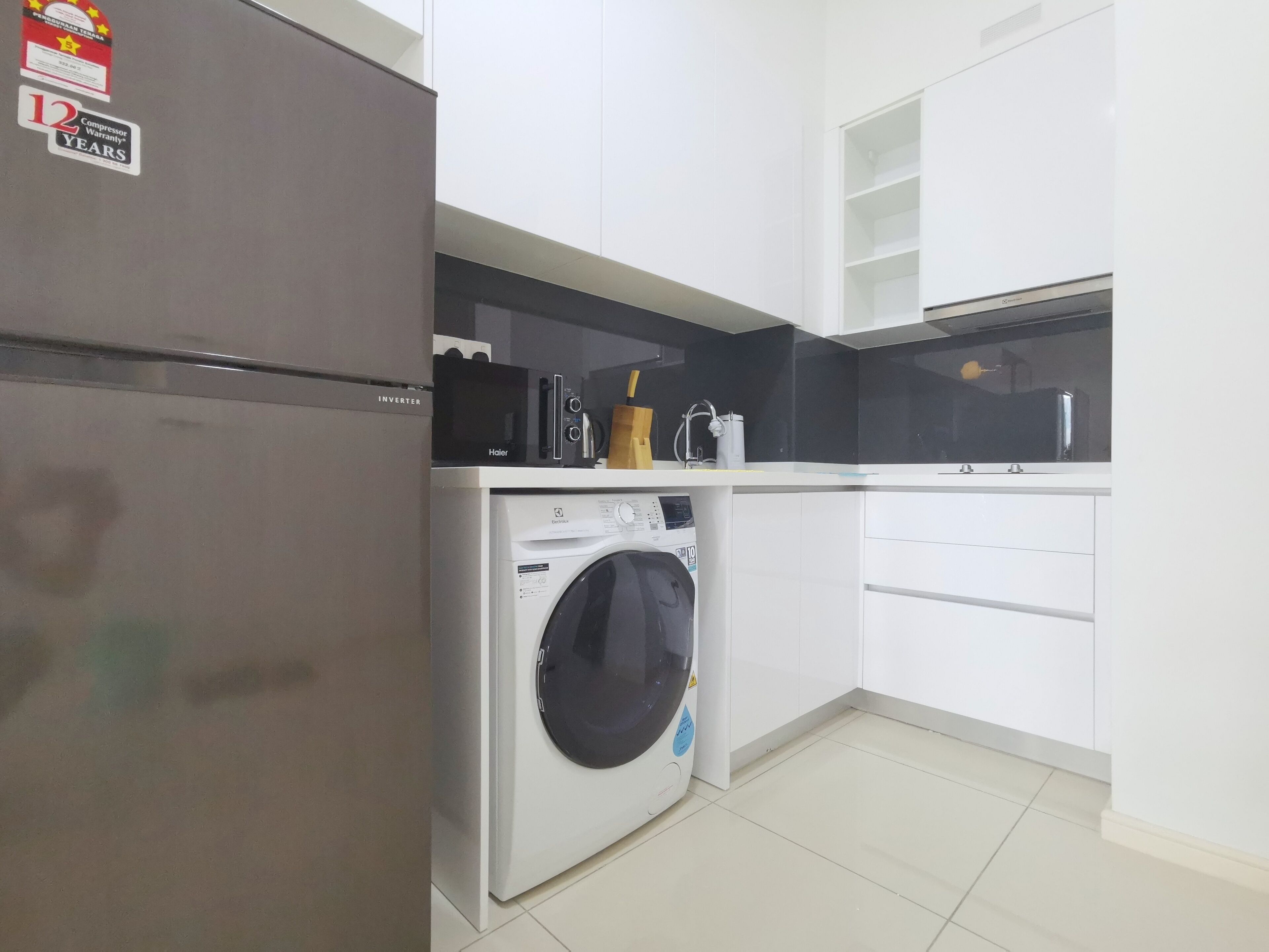 Une cuisine compacte équipée d’un réfrigérateur, d’un lave-linge, d’un four à micro-ondes et d’un petit plan de travail agrémenté d’un bloc à couteaux.