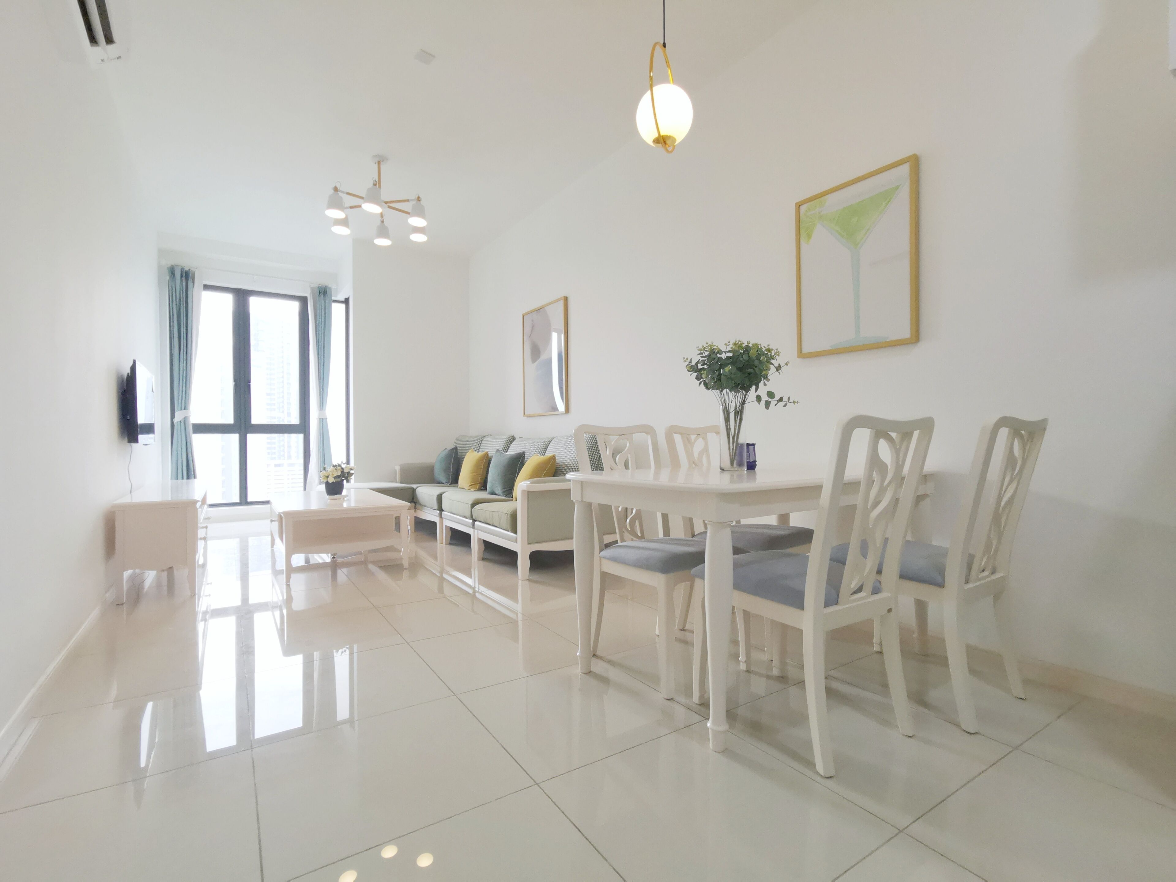 Un salón amplio con una mesa de comedor, sillas, un sofá y un televisor instalado en la pared.