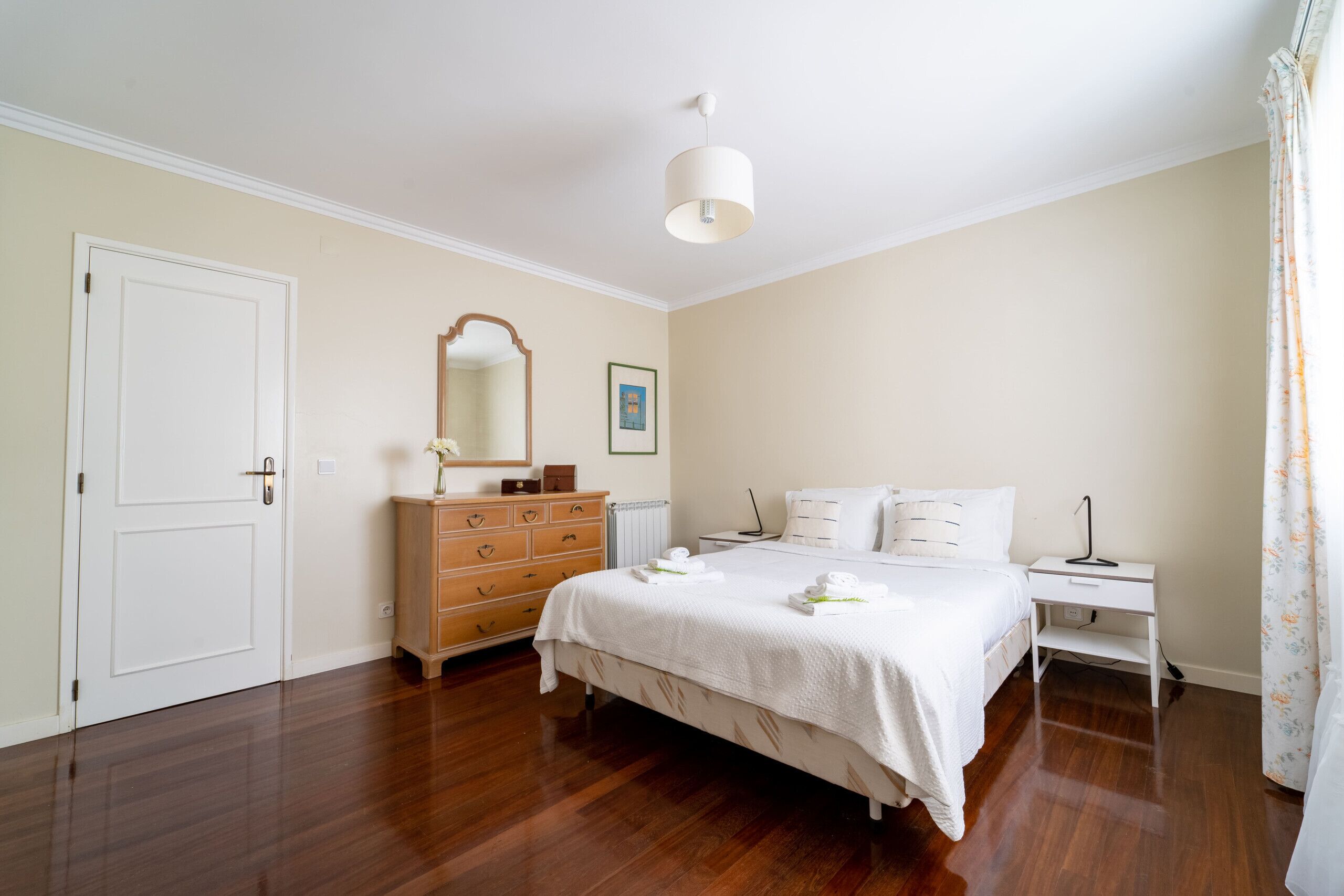 Un dormitorio con una cama grande, un tocador, una mesita de noche, una lámpara y una puerta.