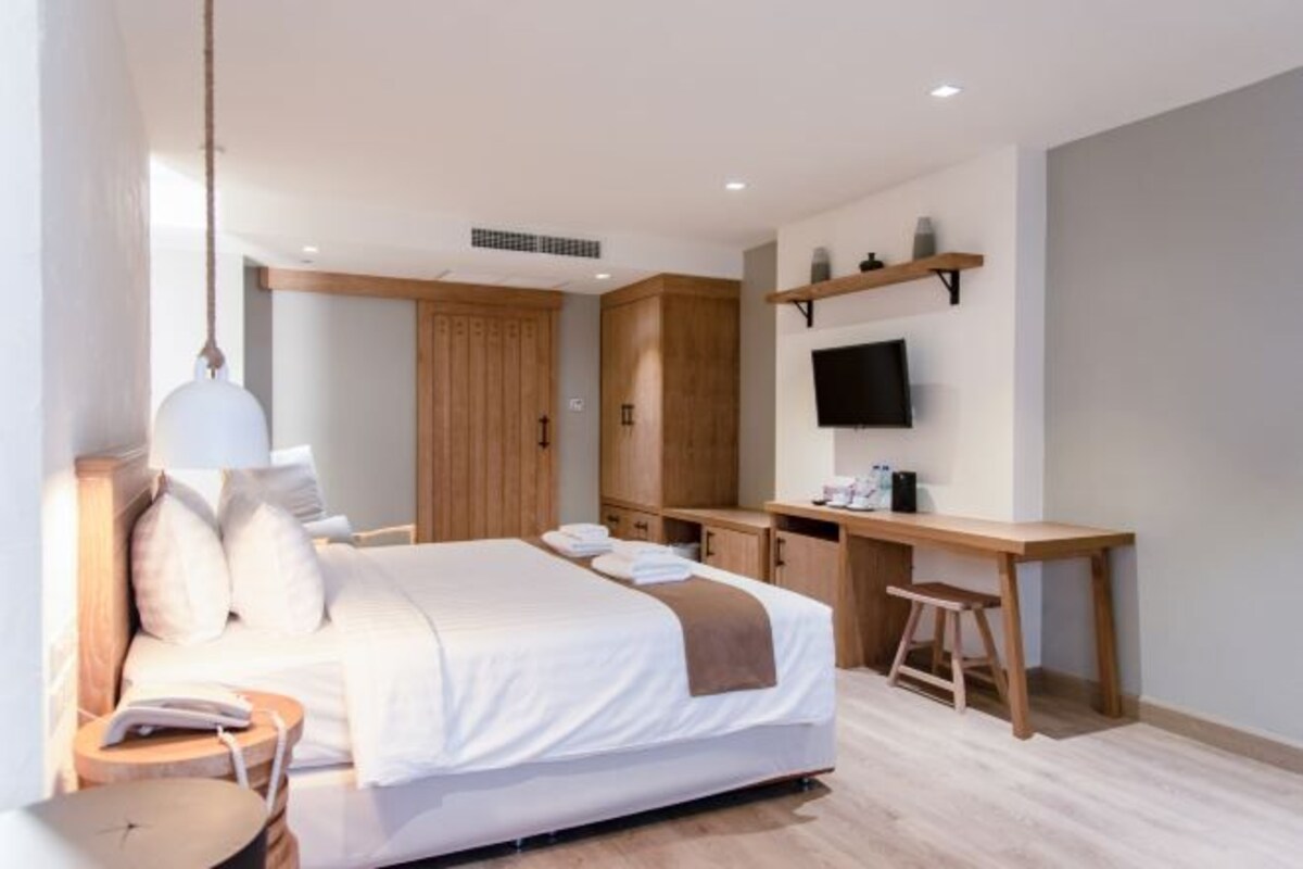 Una habitación de hotel moderna con una cama grande, un escritorio, un televisor y un armario.
