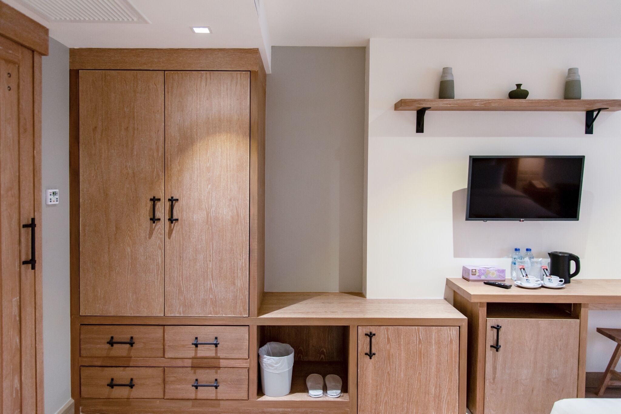 A room with a wooden wardrobe, a desk with a television, and a shelf with decorative items.