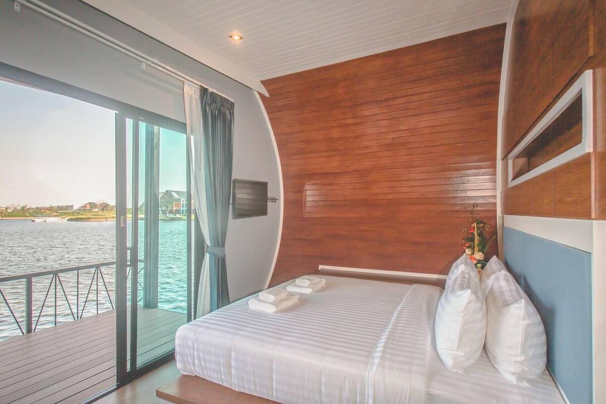A modern hotel room with a large bed, a wooden headboard, a view of the water, and a balcony.