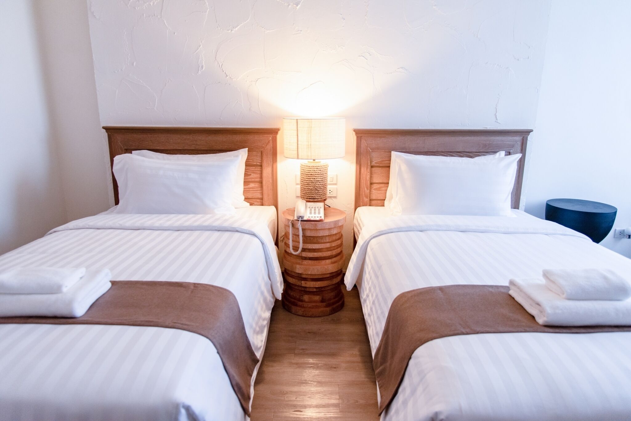 Una habitación de hotel con dos camas, una mesita de noche de madera con lámpara y una mesita auxiliar azul.