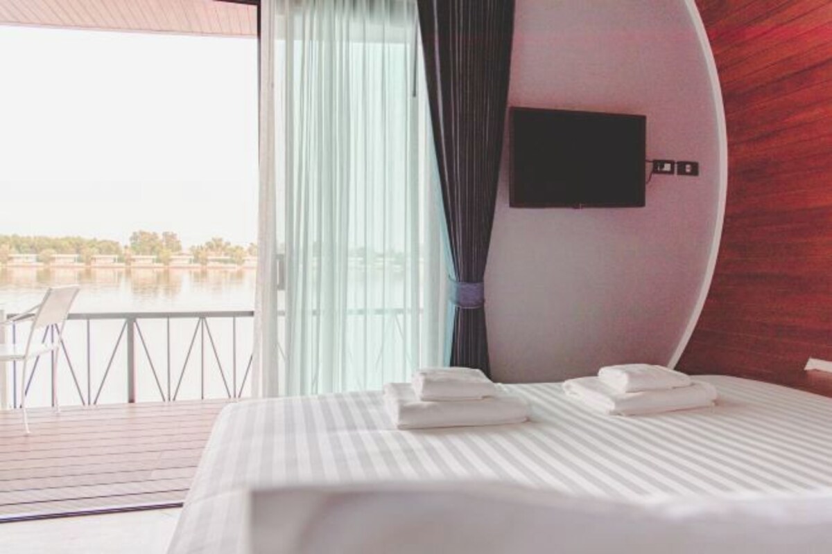 Habitación de hotel con cama, televisor de pantalla plana en la pared y balcón con vista al agua y edificios.
