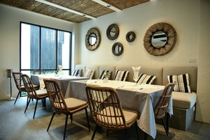Uma sala de jantar com cadeiras de vime e um sofá, uma janela ampla e espelhos fixados na parede.