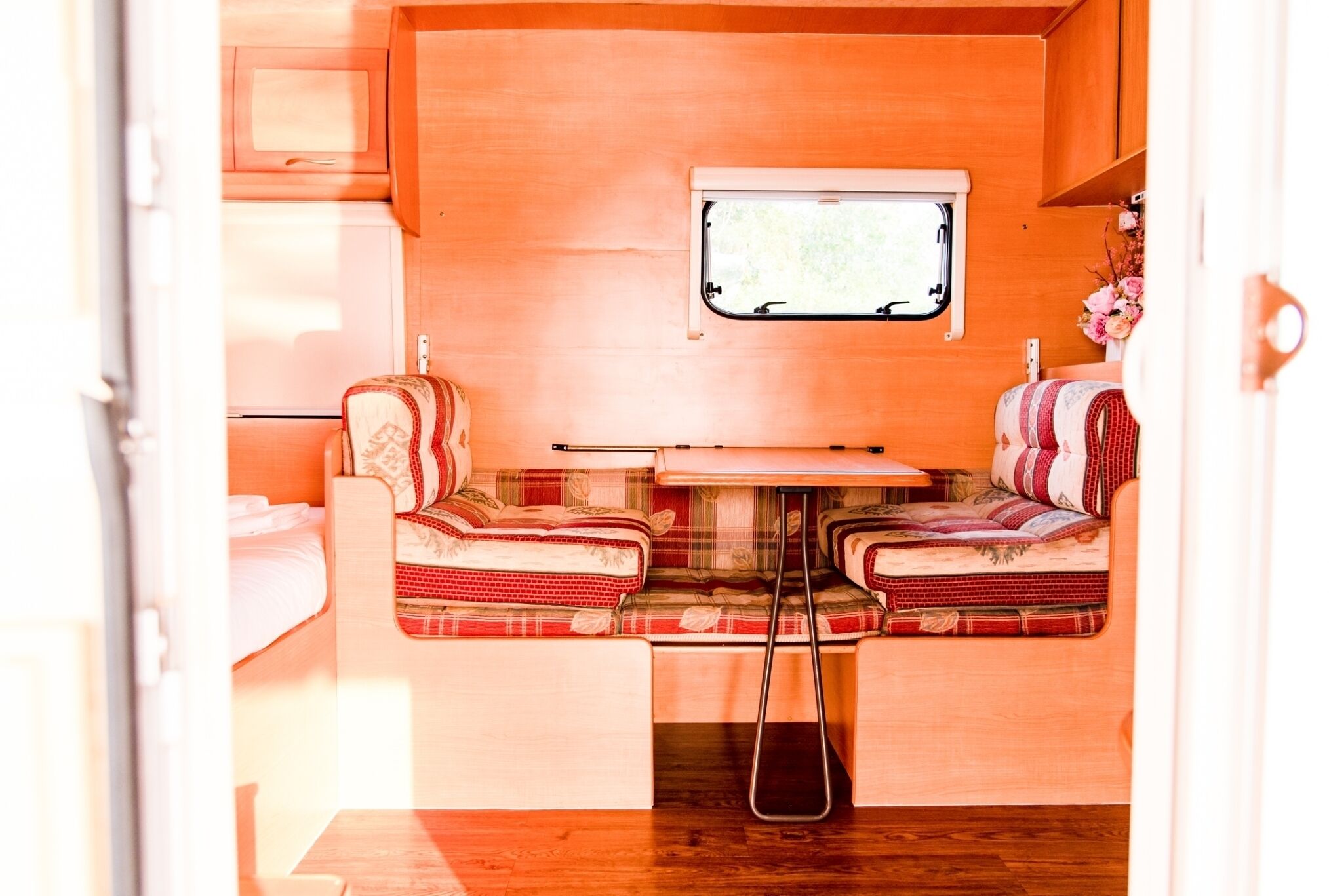 A compact RV interior with a kitchenette, a small dining area, and a window providing natural light.