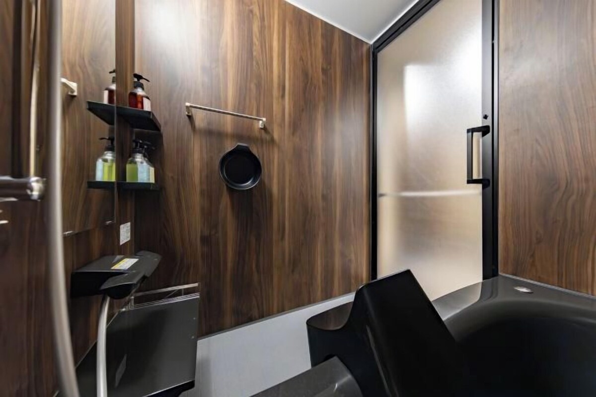 A modern bathroom with wooden walls, a black bathtub, and a shelf with toiletries.
