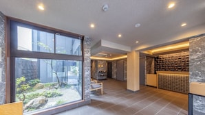 A modern hotel lobby with a large glass window, a reception desk, and a seating area. - MADOKA Kyoto Station West (Kyoto)