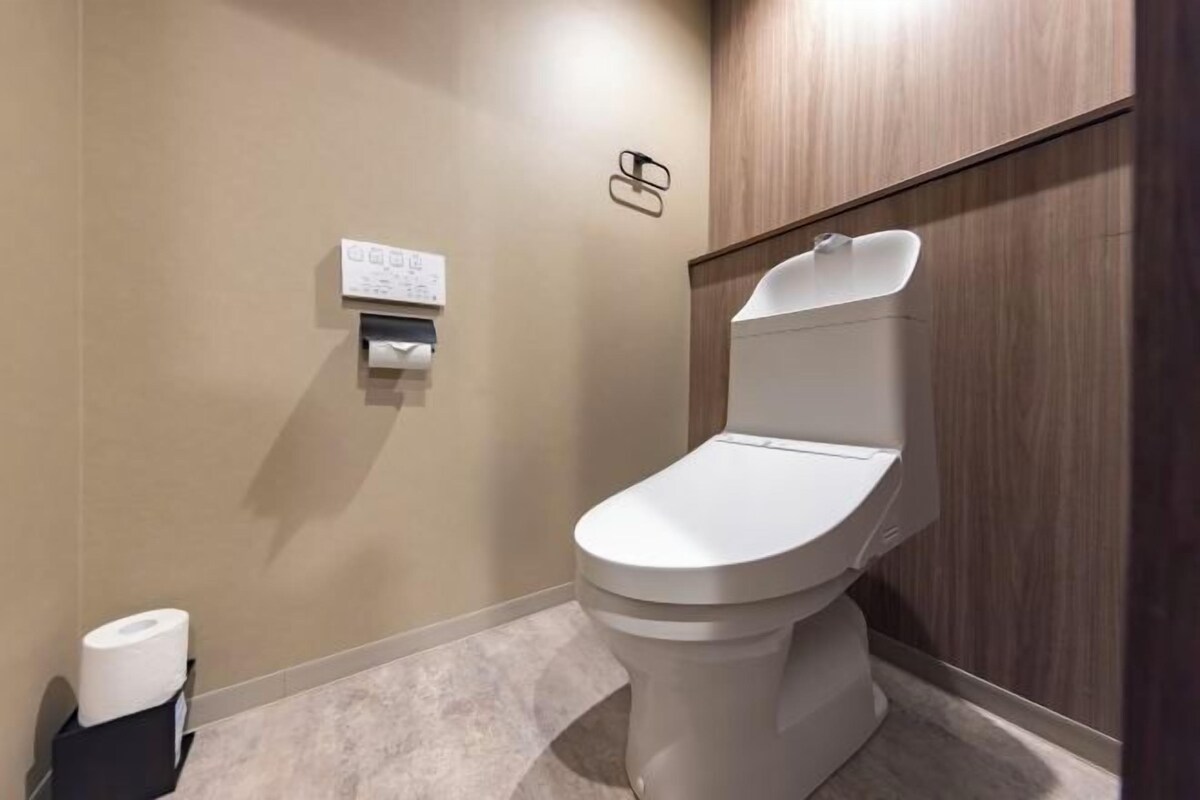 A modern bathroom with a toilet, a paper towel dispenser, and a wall-mounted toilet paper holder.