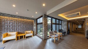 A modern hotel lobby with a seating area featuring sofas and chairs, a marble wall with geometric patterns, large windows, and a tiled floor. - MADOKA Kyoto Station West (Kyoto)