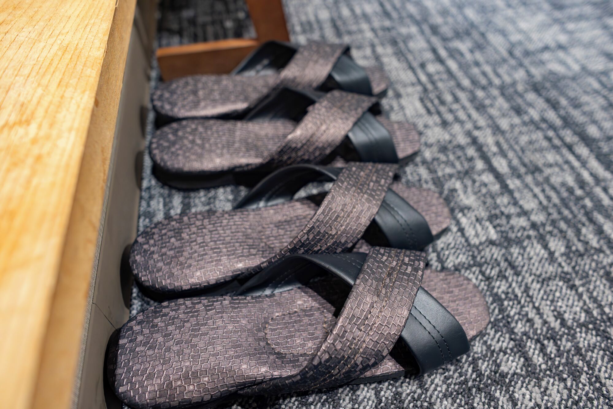 A pair of sandals with a textured pattern, placed on a carpeted floor next to a wooden bench.