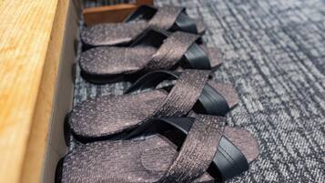 A pair of sandals with a textured pattern, placed on a carpeted floor next to a wooden bench.