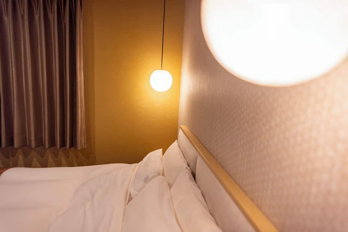 A hotel room with a bed, a hanging light fixture, and a curtain.