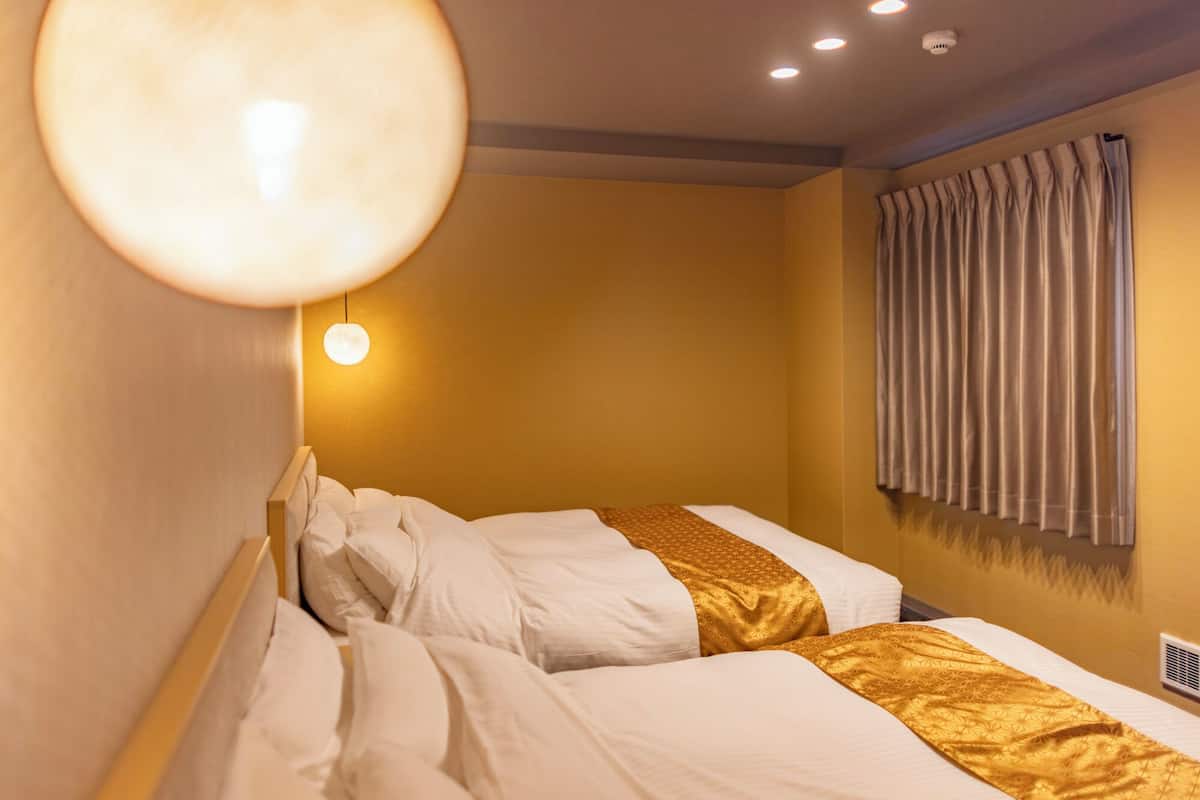A hotel room with two beds, a large round light fixture, and a window with curtains.