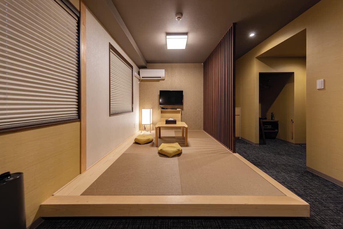 A hotel room with tatami mats, a television, a desk, and a sliding door leading to another room.