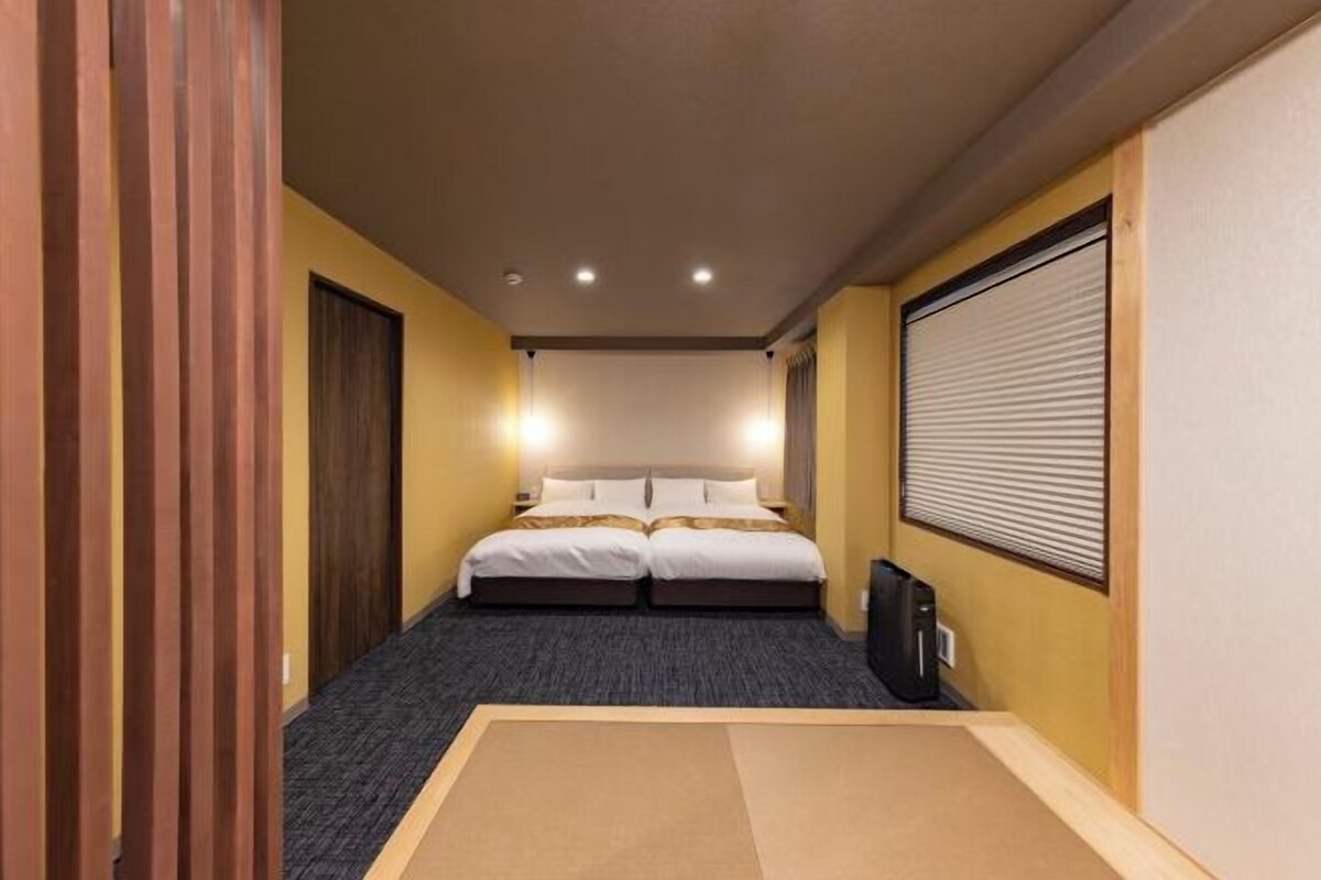 A hotel room with a bed, a desk, and a window with blinds.