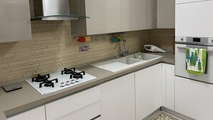 A modern kitchen with white cabinets, a stainless steel range hood, a gas stove, a sink, and a small oven. - D&D vacation home in the center of Mattinata (Mattinata)