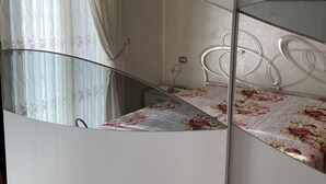 A bedroom with a mirrored wardrobe, a bed with floral bedding, and a nightstand with a lamp. - D&D vacation home in the center of Mattinata (Mattinata)