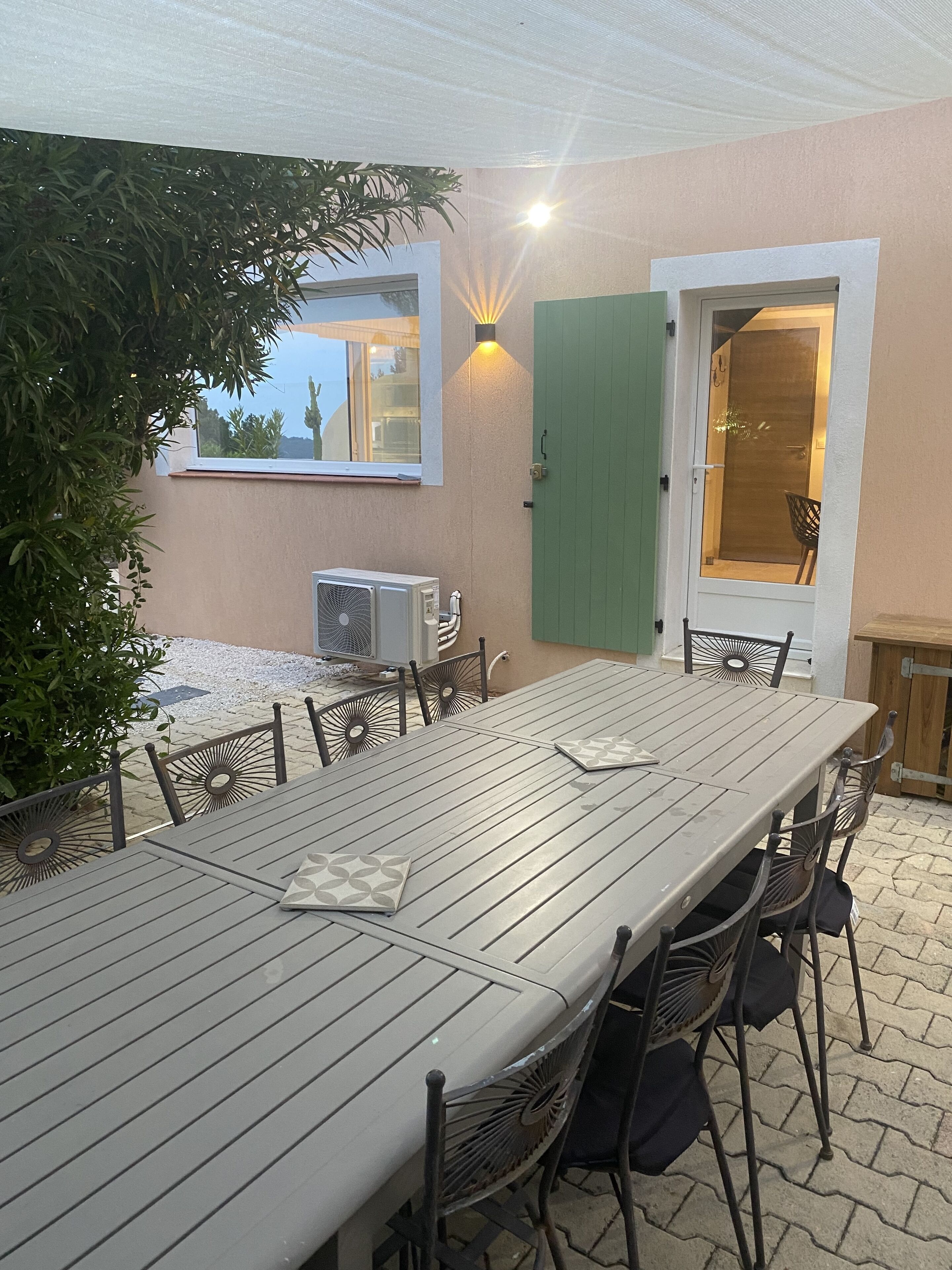 A patio with a long table and chairs, a green door, and a wall-mounted air conditioning unit.