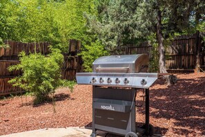 A portable NEXGRILL barbecue grill with multiple burners, set on a gravel surface with a wooden fence and trees in the background. - Stunning Views, Patio, Beautiful Contemporary Home! (Sedona)