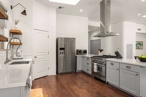 A modern kitchen with stainless steel appliances, wooden shelves, and a large window.