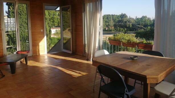 Comedor con mesa y sillas de madera, una lámpara de araña y vistas al exterior con vegetación.