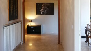Un pasillo con un arco de madera, un radiador, una lámpara de pie y un cuadro con la imagen de un león en la pared.